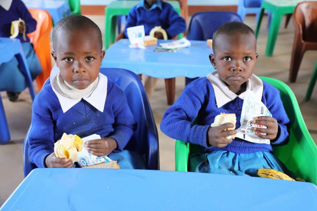 Two pupils eating bananas, bread and milk at their classroom tables